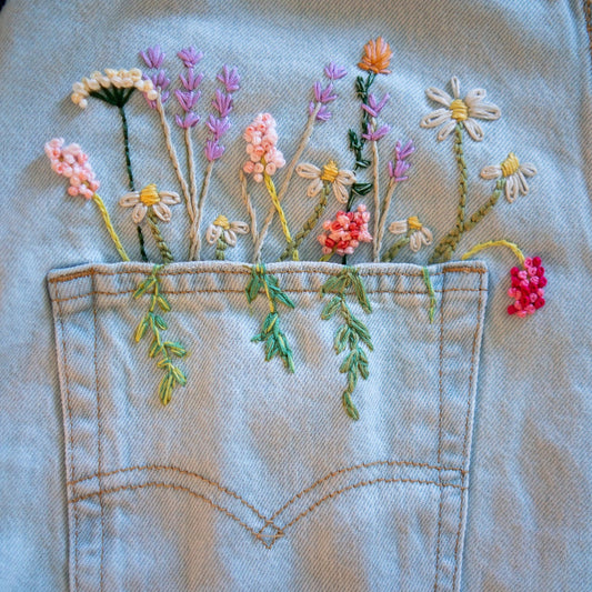 Close-up of a light blue denim pocket with embroidered wildflowers in pink, purple, white, yellow, orange, and green stitched onto the pocket.